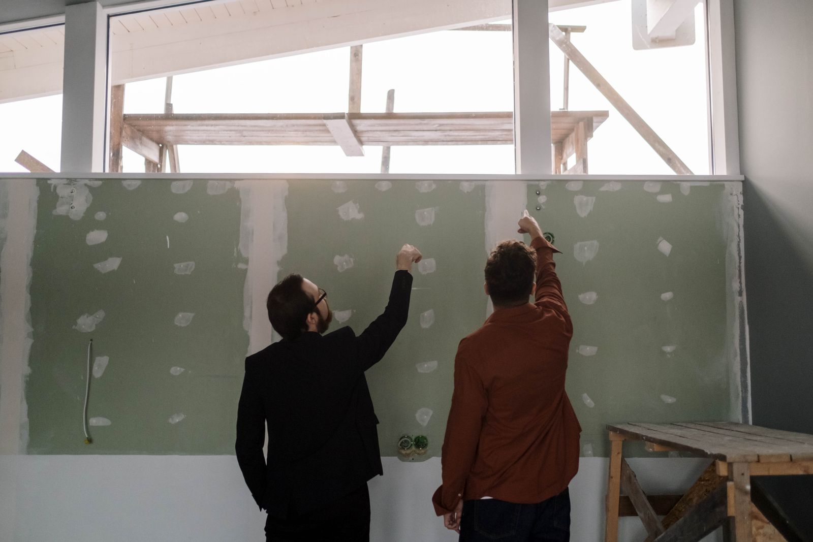Two tradespeople reviewing an interior wall during a fitout — the kind of coordination conversation that often happens reactively, not in the schedule