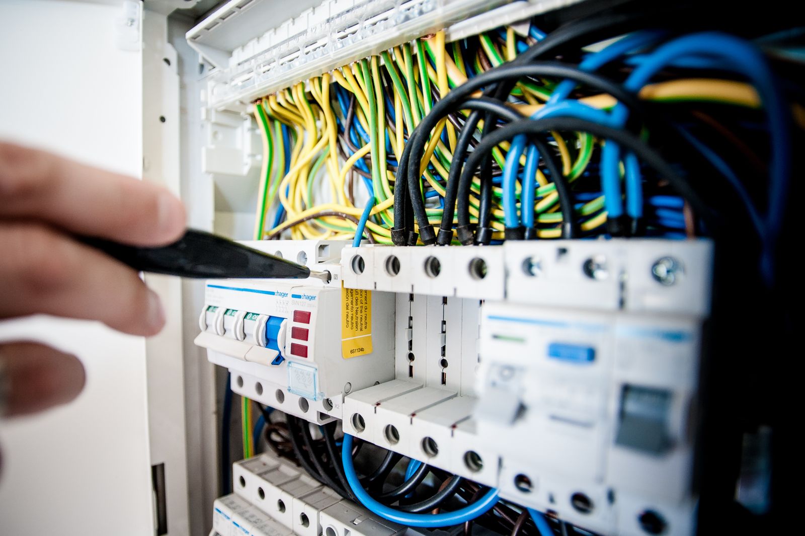 Electrician working inside an open switchboard — the kind of job where the CES paperwork sits in a notebook for days