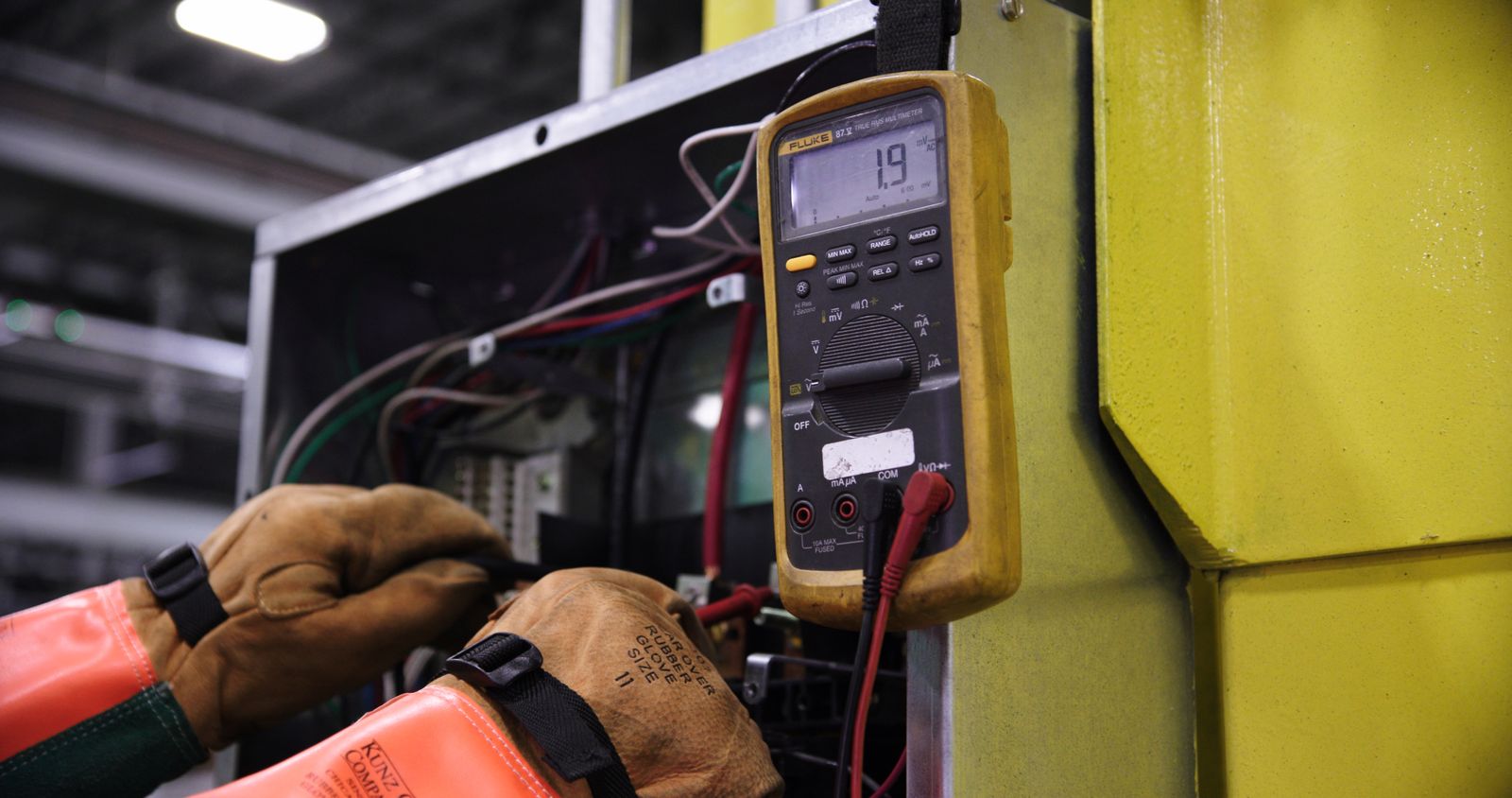 Electrician diagnosing an industrial control panel with a multimeter — the kind of technical work that needs skill-tiered quoting