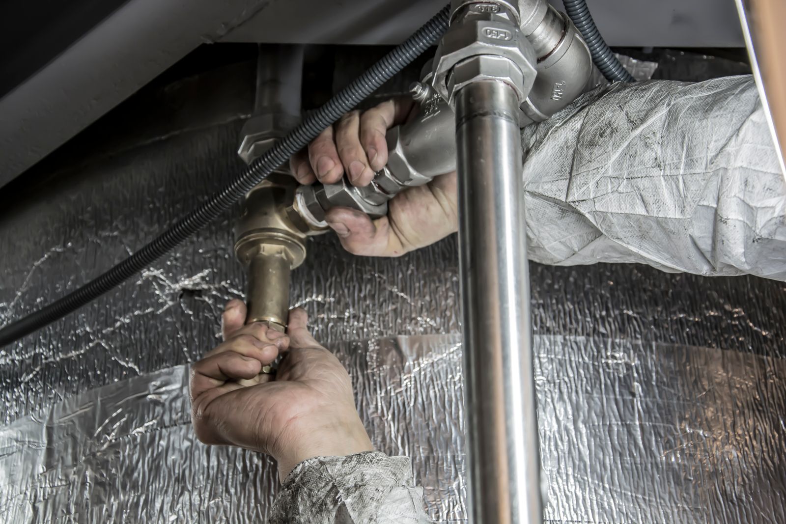 Plumber installing pipe fittings — the kind of job where compliance paperwork ends up on a back-of-the-ute notebook